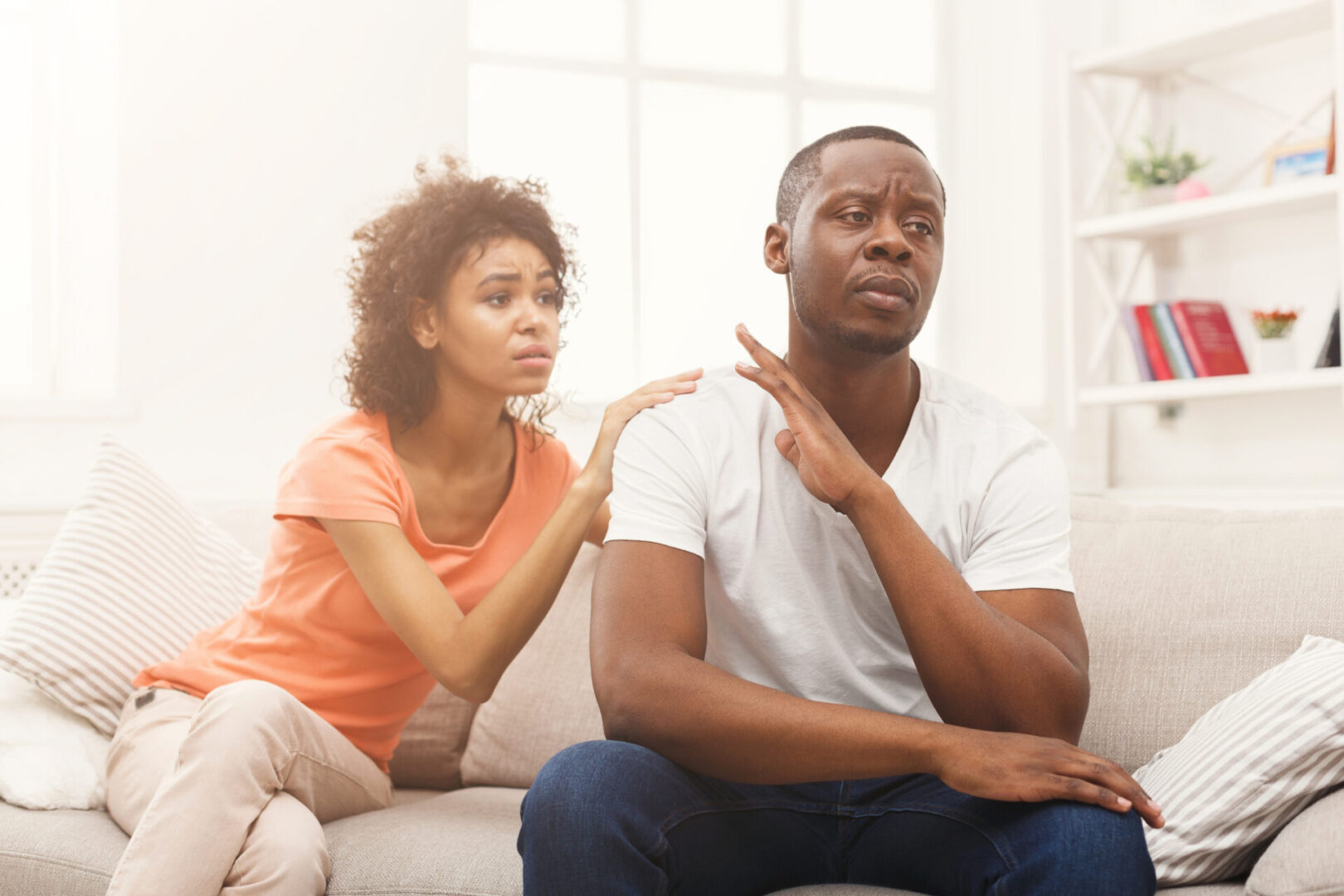 Young african-american couple making peace after quarreling at home, man still feeling offended. Family relationship difficulties concept, copy space