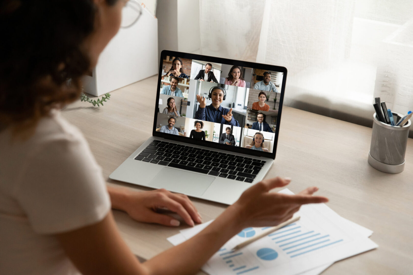 Back view of female employee talk speak on team video call with diverse colleagues coworkers. Woman worker have webcam digital virtual conference at home office, engaged in online group meeting.